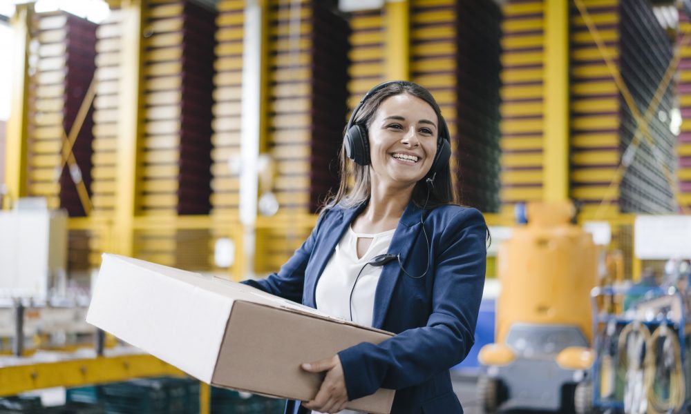 Young woman working at parcel service, carrying parcel in warehouse